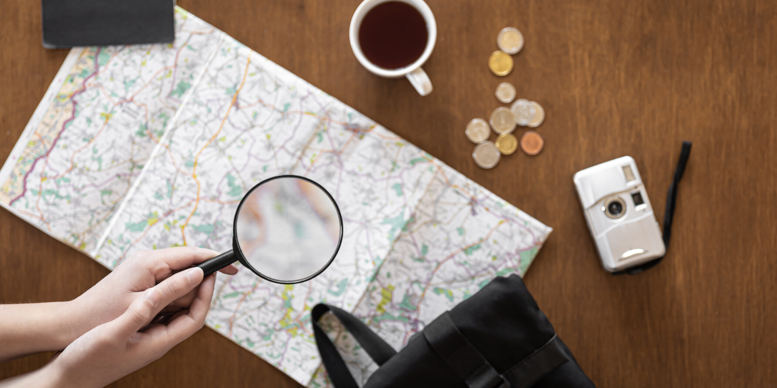 Flat lay, travel planning, trip, map and magnifying glass in female hands.